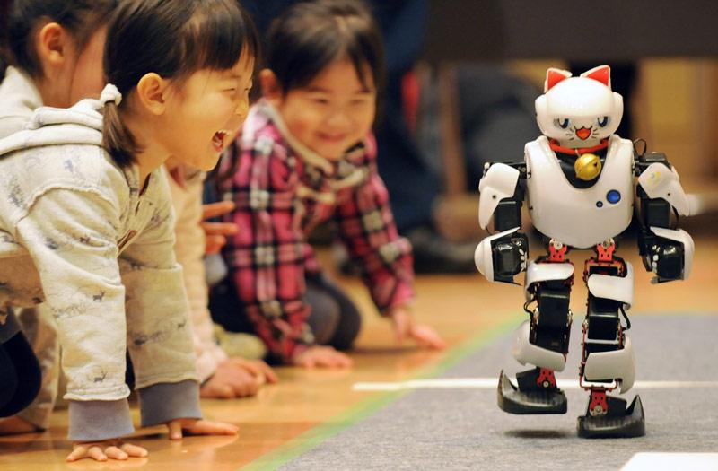 Dimanche 30 janvier, dans un salon de Tokyo, ces petites filles observent, en souriant, un chat-robot. 