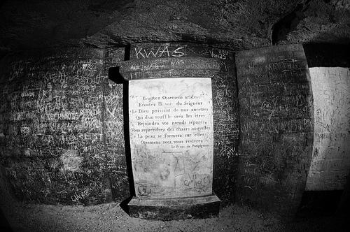Drôle d'endroit pour une visite.... Un panneau et des inscriptions sur les murs des catacombes de Paris