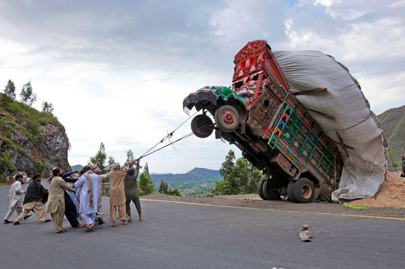 Rodéo mécanique. Ils sont plus d'une dizaine, mais arriveront-ils à remettre sur ses roues ce camion sur chargé? Jusqu'ici, pourtant, tout allait pour le mieux. Son chauffeur roulait tranquillement sur la route montagneuse de Dargai, dans le district pakistanais de Makaland, à environ 160 kilomètres d'Islamabad, la capitale. Il savait que, comme d'habitude, son patron avait chargé sa remorque de fourrage jusqu'à l'extrême limite. Mais cela ne l'inquiétait pas.AuPakistan, c'est souvent la règle. Les camions sont fatigués, les normes inexistantes, mais la science des «chargeurs» fait des miracles. Jusqu'à ce virage en épingle et cette marche arrière de trop quiaprovoqué l'accident bête: la chute en arrière… Et cette scène de rodéo mécanique faceàuncamion cabré.