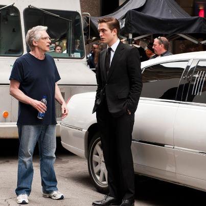 Photo : Interviews de Robert Pattinson et David Cronenberg avec The Miami Herald, Salon.com et The Boston Globe! (Via le RpattzClub) • The Miami Herald : David Cronenberg se souvient de la fois où Oliver Stone lui a demandé, “David, ça t'embête d'être un réalisateur si marginal ?” Ce à quoi Cronenberg, une des réalisateurs le plus admiré et le plus célèbre au Canada, a répondu, “Oliver, ça dépend. De combien de public as tu besoin?” C'est là la clé secrète du succès de Cronenberg. Cosmopolis, con nouveau film qui sort vendredi, est une adaptation du roman de Don DeLillo sur un jeune milliardaire Eric Packer qui passe une journée dans sa limousine à se promener dans New York dans le but de se faire couper les cheveux. Il n'y a pratiquement pas d'intrigue traditionnelle dans Cosmopolis. Plus de la moitié du film se déroule dans une limousine, où Eric a des rendez vous avec son personnel, subit un checkup de son docteur (“Votre prostate est asymétrique”) et il y fait même l'amour. Bien qu' Eric soit incarné par Robert Pattinson, la star hautement populaire de la saga Twilight, Cosmopolis est dur à vendre pour le public des complexes multisalles— un film rigoureux et étrangement hypnotique rempli de dialogue dense, avec beaucoup de jargon. A 69 ans , Cronenberg continue de faire ses films grisants de la manière forte. “Quand vous êtes un réalisateur, vous passez un an et demi de votre vie — peut être plus— à assembler des choses : vous devez mettre en place votre financement et vous cherchez des acteurs qui vont vous rejeter” dit il “C'est un processus difficile. Donc le film doit réellement susciter l'excitation et m'intriguer et me donner l'impression que je vais découvrir quelque chose en le réalisant ” ajoute t-il. “Naturellement, il vous faut tailler un budget qui correspond au thème. Personne ne va dépenser $200 million pour Cosmopolis. Mais si vous êtes réaliste sur vos attentes et la taille de votre public, et que vous voulez travailler pour peu d'argent, vous pouvez proposer des choses intéressantes.” Le prix de Cosmopolis est de $20 million et semble assez élevé pour un film qui ne fera pas partie du Box Office , mais Cronenberg a compensé le risque pour les financiers en choisissant Pattinson, qui apparaît dans toutes les scènes (Colin Farrell devait au départ jouer Eric, mais a dû se rétracter à cause de soucis de planning.) “J'ai eu le script à l'improviste et on m'a offert le rôle, ce qui était un peu choquant,” dit Pattinson “D'habitude, les films qu'on me propose directement sont terribles. Ce script semblait si original, c'était presque rutilant. “Je savais qu'on pouvait faire un film. J'étais juste soucieux de ne pas être celui qu'il fallait. Je ne cessais de me dire ‘Il y a des tonnes de personnes bien meilleures que moi pour ce rôle!’ Ca m'a pris un moment d'accepter cette idée.” Cosmopolis a offert à Pattinson l'opportunité d'essayer un jeu d'acteur assez minimaliste et il ne l'avais jamais fait avant. Eric Packer est un homme détaché , distant qui exprime rarement ce qu'il ressent . Sur la page, DeLillo nous ouvre ses pensées et ses monologues intérieurs ; à l'écran, Pattinson utilise de petits gestes, la trace la plus fine d'un sourire ou un sourcillement ou le durcissement d'un regard pour faire passer son état. “Au début du film, je portais ce costume noir , immaculé,” dit il. “Je porte des lunettes complétement noires et je suis immobile, je ne bouge pas. Tous les outils que les acteurs utilisent pour leur performance m'avaient été enlevé,” dit il. “Mais je me sentais en sécurité car je savais que David me regardait — m'observait vraiment — et ça vous donne confiance. La plupart du temps , sur les plateaux de cinéma, je me demande si le réalisateur fait vraiment attention à ce que je fais” La légion de fans Twilight de Pattinson va être confus par ce film froidement fascinant , mais Cronenberg a suffisamment de fan pour s'assurer un public pour cette mixture étrange. Tout le monde n'aimera pas, bien entendu. Il n'y a pas un fan de Cronenberg sur la planète qui peut dire en toute honnêteté qu'il adore tous les films du réalisateur. Et c'est un hommage aux risques qu'il prend depuis le début de sa carrière de 37 ans Pour Cronenberg, également, l'inspiration d'adapter Cosmopolis n'est pas venu des grands thèmes mais de subtiles détails “J'ai simplement été emporté par les dialogues. C'est un peu comme du David Mamet ou Harold Pinter, car c'est réaliste à un niveau— ça ressemble à la façon dont les gens parlent—mais c'est aussi très stylisé. Quand je les ai transcris sous la forme d'un script, ça a donné au film une cohésion et une résonance incroyable. C'est à ce moment là que je me suis demandé, ‘Est ce un film’ . Et je me suis dit , ‘Oui. C'est un film vraiment intéressant.’” Presque tous les dialogues viennent du livre, ce qui signifie que les acteurs devaient sembler naturels en disant des répliques comme “Nous sommes tous jeunes et intelligents et on a été élevé par des loups. Mais le phénomène de réputation est une chose délicate. Une personne s'élève en un mot et s'effondre en une syllabe.” Pour Pattinson, les cadences inhabituelles et les choix des mots ont été libérateurs. “J'ai ressenti une connexion physique avec l'écriture— je trouvais ça tellement bien— et je voulais le lire à voix haute dès que j'ai eu le script, juste pour voir comment ça sonnait. C'est écrit de manière tellement parfaite. J'ai adoré le fait que je ne devais pas mettre mon empreinte personnelle sur cela en tant qu'acteur. Je devais juste faire ma performance de la façon la plus honnête possible.” • Salon.com (D. Cronenberg) : Bien entendu tout le monde veut vous poser des questions sur votre star, qui malheureusement a décidé de ne pas se joindre à nous aujourd'hui. Je suppose qu'il a ses raisons. Comment et pourquoi avez vous décidé de choisir Robert Pattinson? Ca a débuté de façon pragmatique. Vous avez une liste de 10 personnes de la part de divers producteurs et d' agents, et vous débutez avec les bases. Quel âge a le personnage? Et quel âge a l'acteur? . Ce personnage est jeune, on lui donne 28 ans. Donc vous commencez par là. Semble il être celui qu'il faut? Eric parle beaucoup de musculation et est très physique, donc vous n'allez pas choisir quelqu'un qui est en surpoids. On commence avec des choses aussi simple . Et puis vous passez aux choses pragmatiques : Avez vous un gros budget et de quelle star avez vous besoin pour que votre film soit financé ? Et voilà une chose auquel les gens ne pensent pas, c'est la passeport de l'acteur. C'est une co-production Franco - Canadienne, donc vous êtes vraiment restreint sur le nombre d' Américains que vous pouvez avoir. Il n'y a qu'un seul américain dans le film , même si ça passe à New York, et c'est Paul. Donc le fait que Rob soit anglais a été une aide, car il pouvait correspondre à la co-production . La route est donc longue, et enfin vous vous demandez : Le mec a t-il le talent , le charisme pour pour porter le film? Car ce personnage est dans toutes les scènes du film, sans exception, et c'est très inhabituel , même pour une star. Donc j'ai regardé tout ce que j'ai pu trouver sur ce que Rob avait fait, y compris “Little Ashes,” où il incarne le jeune Salvador Dali, et je me suis dit qu'il pouvait le faire. Et je pense qu'il est vraiment extraordinaire. Enfin, il y a mon intuition, et le casting est une partie importante de la réalisation qui est vraiment invisible. Les documentaires sur le Making-of ne couvre pas souvent le processus de casting, mais pour un réalisateur, c'est une partie fortement importante de votre art. Vous jonglez avec toutes les autres balles dont je vous ai parlé et vous trouvez l'homme qu'il vous faut Je me rend compte que je ferais mieux de ne pas vous poser cette question, mais pensez vous que Rob ait hâte de changer son image après “Twilight,” et se lancer dans des personnages complétement différent? Après ce rôle, et après avoir incarné un sociopathe sadique dans“Bel Ami,” on dirait qu'il prend ce chemin. Je sais après avoir fait des interviews avec lui en Europe qu'il ne pense pas vraiment en terme de carrière. Trucs ennuyeux. Il est toujours intéressé par le fait de faire des choses inhabituelles. Il vous dirait que lorsqu'ils ont débuté le tournage de “Twilight,” il pensait que c'était un film indépendant. C'était en quelque sorte le cas ! Le film avait Catherine Hardwicke pour réalisatrice , et c'était une histoire de vampire un peu tordu et inhabituelle. Personne ne savait que ça deviendrait ce succès planétaire qu'il est devenu. Dans un sens “Cosmopolis” est bien plus proche de son coeur que “Twilight”. Quant il a lu le script, il m'a dit que lui aussi avait été frappé par les dialogues. Il trouvait ça incroyablement frais et nouveau et surprenant et engageant , et il a immédiatement voulu le faire. Il avait peur car je pense qu'il n'a toujours pas accepté le fait qu'il est vraiment acteur! Il n'a pas grandi en se disant qu'il voulait devenir acteur. Comme avec de nombreux acteurs, et pas uniquement les jeunes acteurs, ceux qui n'ont pas d'expériences , il n'était pas sûr d'être assez bon ! Il n'était pas sûr d'être la bonne personne, et il ne voulait pas être celui qui ferait merder ce superbe projet. Donc mon travail, à ce moment là, a été de le convaincre qu'il était en effet la bonne personne. Je crois que ça m'a pris 10 jours . Vous me dites que vous avez vraiment vu les films “Twilight”? C'est un peu dur à imaginer. Oui — ou non, j'en ai regardé un et demi. Je m'intéresse à tout, franchement. Je ne suis pas un snob vous savez. Je suis très curieux de tout. Si quelque chose est hautement populaire, ça ne veut pas forcément dire que je vais le regarder mais parfois, je suis curieux de savoir pourquoi quelque chose est vraiment populaire. Dans le cas de “Twilight,” je l'ai regardé pour Rob, c'était pour ça. Ce n'est pas comme si.... je ne les avais pas vus avant • The Boston Globe : Robert Pattinson, David Cronenberg , un bon duo Le réalisateur culte David Cronenberg et la star principale de“Twilight”Robert Pattinson a sonné la cloche pour l'ouverture de la Bourse de New York la semaine dernière pour promouvoir leur nouveau thriller psychologique “Cosmopolis.” Les deux hommes s'accordent à dire que leur visite était un peu étrange . Après tout, “Cosmopolis,” adapté du roman de Don DeLillo, est une critique capitaliste qui , bien que publié en 2003, parle du mouvement Occupy Wall Street et crée un portrait perturbant du vide des 1%. L'acteur anglais et le réalisateur canadien , qui nous ont appelé peu de temps après que Pattinson ait fait une apparition hautement médiatisé au “Good Morning America,” ont admis que leur expérience “Cosmopolis” a été parfois étrange et, tout comme leur film , inconfortable avec une pointe d'ironie. Il y a l'étrangeté du film même . Puis il y a les fans de “Twilight” qui adorent assez Pattinson pour aller voir un film R-rated sur l'économie qui implique que l'excentrique milliardaire subisse un examen de proctologie à l'arrière d'une limousine. Ajouter à cette étrangeté l'implication de Pattinson dans un scandale très public de tromperie sa petite amie de longue date Kristen Stewart s'est récemment excusée pour avoir été infidèle avec Rupert Sanders, le réalisateur de “Snow White and the Huntsman.” Après cette révélation publique de Stewart, Pattinson a disparu pendant des semaines, la rumeur disait qu'il était chez Reese Witherspoon, puis il a refait surface, pour le plaisir des paparazzi, pour promouvoir“Cosmopolis” sur les tapis rouges et ailleurs Ca a été un voyage étrange, mais Cronenberg et Pattinson semblent merveilleusement à l'aise — du moins ensemble — parmi toute cette maladresse. Q. Vous avez tous les deux dit que vous aviez tourné le film de manière chronologique et je sais que dans de nombreux films, les dernières scènes sont tournées en premier. Etait ce un luxe de tourner dans l'ordre ? Cronenberg: Une des choses les plus difficiles était que je devais apprendre en tant que réalisateur ce que c'était exactement. Tout à coup vous êtes obligé de tourner la dernière scène du film en premier. Et c'est dur pour les acteurs car ils ne savent pas encore qui ils sont et ils tournent leur scène de mort. En tant qu'acteur, j'étais moi même dans le film de Clive Barker “Nightbreed,” et la 1ère chose que nous avons tourné était mon personnage se faisant tuer. Et j'ai dit une chose typique pour un acteur. J'ai dit 