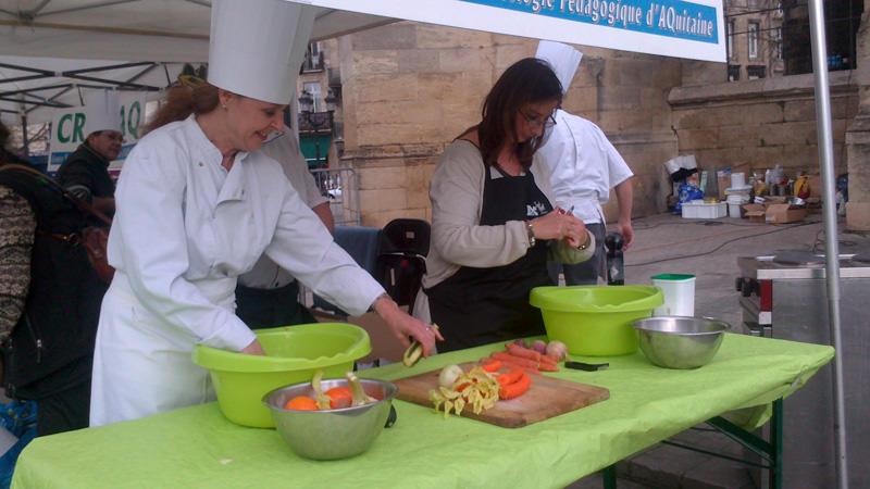 DSC_0040 Une cuisinière en toque et une bénévole pèlent des légumes.