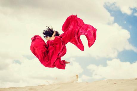 fille brune dans une longue robe rouge sautant d'une dune par Dasha Kond 