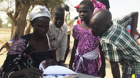 À Leer, des personnes à la recherche de leurs proches feuillettent un livre avec des photos d'enfants sud-soudanais qui se trouvent dans les pays voisins. CC BY-NC-ND/ICRC/Pawel Krzysiek