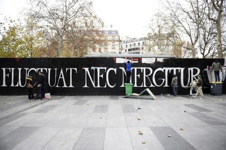 Members of a group of street artists paint a mural reading Paris' motto 
