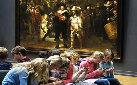 Un groupe de lycéens au Rijksmuseum d’Amsterdam toiurnant le dos à la La Ronde de nuit de Rembrandt. En fait, ils consultent l'applicatin éducative du musée sur le tableau.