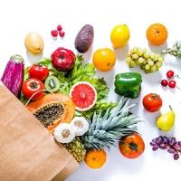 Divers fruits tombent d'un sac en papier sur une table blanche.