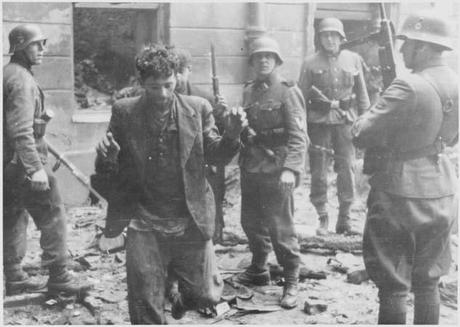 Photo dans une rue pleine de gravats. Deux hommes en civil, hirsutes, lèvent les bras. Ils sont entourés par quatre soldats allemands armés, avec casques, qui les regardent.