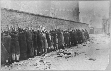 Photo du mur du ghetto : une trentaine de personnes y son collés, tournant le dos, les mains en l'air appuyées sur le mur. Au sol des gravats. On ne voit pas de soldats.