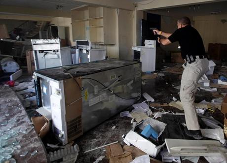 Un garde de sécurité privée dans une maison dévastée par la tremblement de terre vise un homme suspect  (en haut à gauche) montant l'escalier. Crédit : AP Photo/Ramon Espinosa