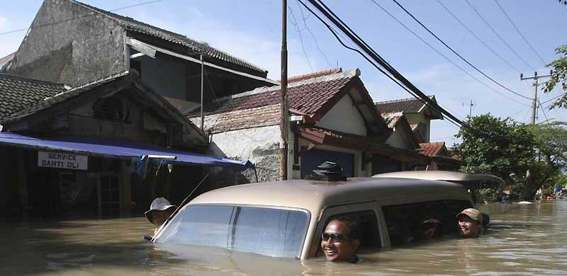 Jeudi 25 mars, à Karawang, en Indonésie. Des habitants poussent, avec le sourire, une voiture dans une rue entièrement inondée après les fortes pluies qui ont frappé cette région ces derniers jours. 