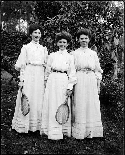 Three young women in light dresses holding tennis racquets