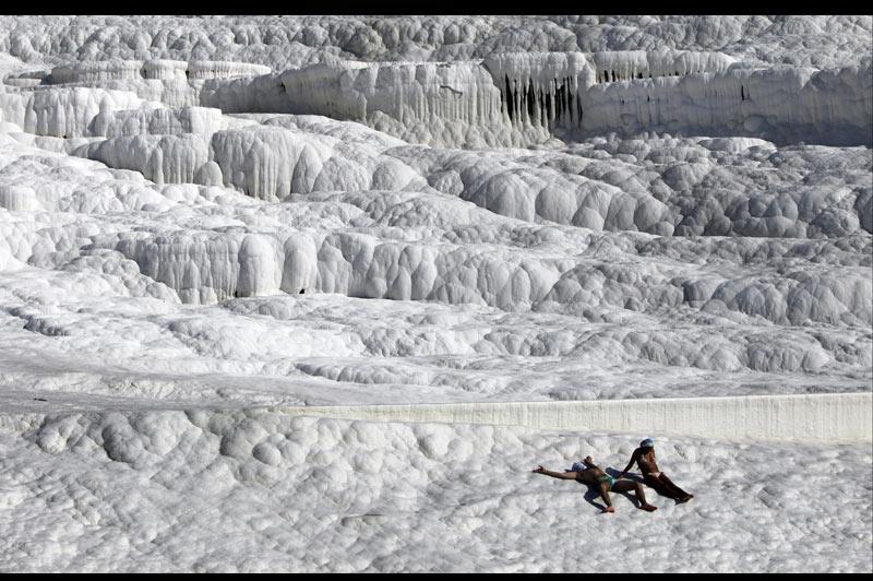 <b></div>OUATE IS IT ?</b> Il a fallu des millénaires à la nature pour dessiner cet endroit, situé en Turquie, en un lieu, Pamukkale, qui signifie «château de coton». Un surnom qui fait évidemment référence à la blancheur éclatante de cette falaise, mais pas à sa douceur, même si elle sert ici de matelas à deux touristes inconscients, déjà rôtis, pas loin d’être carbonisés. Car ils ne sont pas en train de se griller la peau sur de la glace ou du sel, mais sur du calcaire, lentement déposé sous forme de cascades fossilisées et de piscines débordantes de stalactites par des dizaines de sources d’eau chaude, surchargées en sels minéraux et exploitées depuis l’Antiquité pour leurs vertus thérapeutiques. 