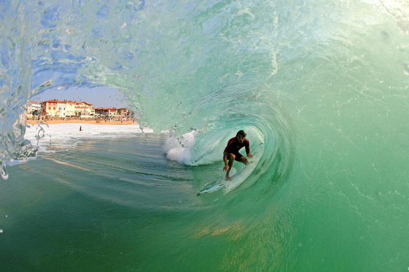 <b></div>LE TUBE DE L’ÉTÉ</b>. Ce n’est pas la taille de ce beach break (littéralement : qui se brise sur le sable) qui nous étonne ni l’habileté de ce surfeur tentant sa chance à l’étape française du championnat du monde. Non, ce qui stupéfie, c’est que le photographe, enfermé dans le tube d’eau juste devant le candidat, ait eu le talent incroyable de saisir l’homme à une nanoseconde du moment où la lèvre de la vague allait se refermer sur lui en un baiser d’émeraude. Pour que le bonheur soit complet, la providence a également permis que soient aperçues, comme dans une longue vue aquatique, les maisons du front de mer d’Hossegor, dans les Landes, où se déroulait la compétition. (Laurent 