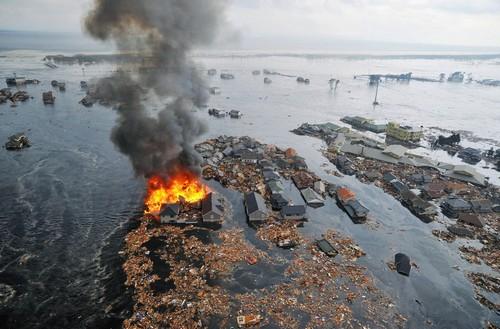 Une maison en flammes entourée par les eaux laissées par le passage du tsunami à Natori