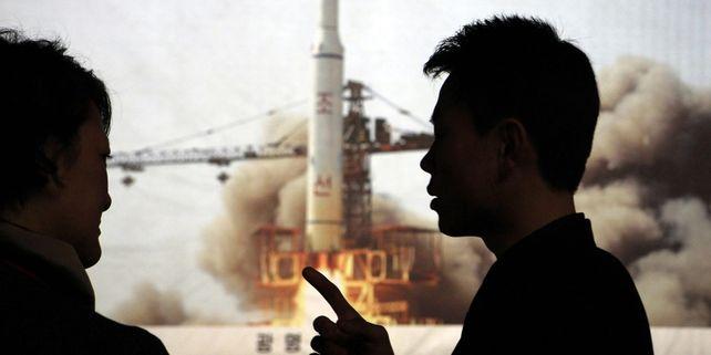 Un guide nord-coréen discute avec une journaliste étrangère devant une photo du lancement de fusée de 2009.