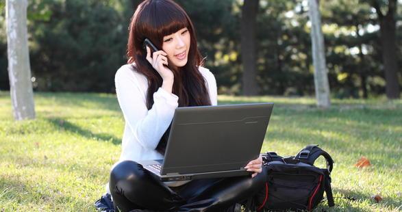 étudiante assise dans l'herbe avec un PC et un smartphone