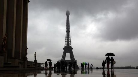 Tourists protect themselves from the rain under umbrellas in front of the Eiffel tower in Paris as they visit the French capital during summer holidays