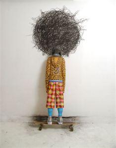 Afro Charlie. 2009 Instalación. Figura de una adolescente a tamaño real, tallada en madera policromada, patineta y dibujo al carbón sobre pared.  