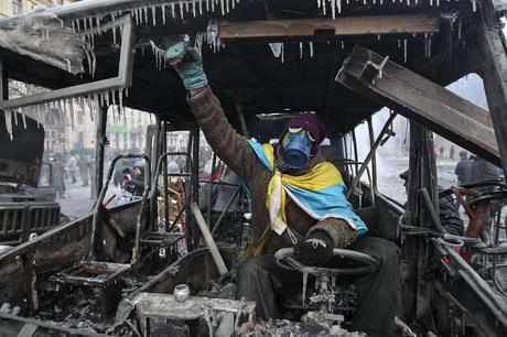 A pro-European integration protester sits in a burnt police bus after a rally near government administration buildings in Kiev