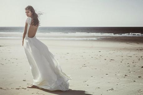 belle femme brune mannequin en robe de mariée laure sagazan, dos décolleté sexy pour le jour de son mariage, voile de mariée long avec couronne de fleurs pics à chignon de fleurs d'organza, mariage sur la plage romantique 
