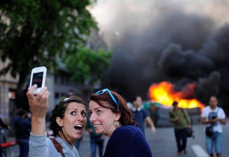 A Barcelone, deux touristes font un selfie devant un container de poubelle en feu.
