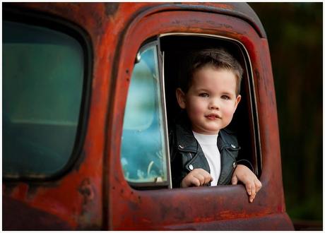 photo de Lisa Holloway représentant une jeune garçon en blouson de cuir noir à travers la fenêtre d'un vieux pick up rouillé