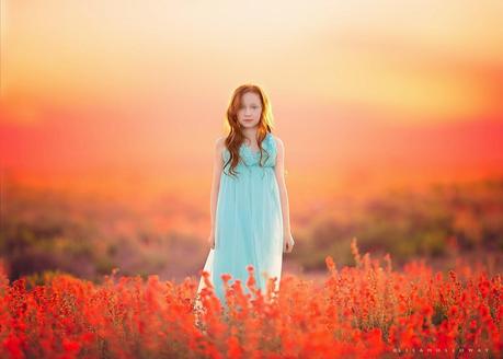 photo de Lisa Holloway représentant une jeune fille rousse en robe bleu pale au milieu de fleurs rouges 