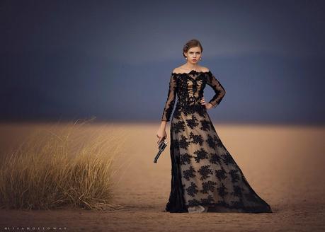 photo de Lisa Holloway représentant une jeune femme en robe noire en dentelle tenant un ancien revolver à la main dans un désert 