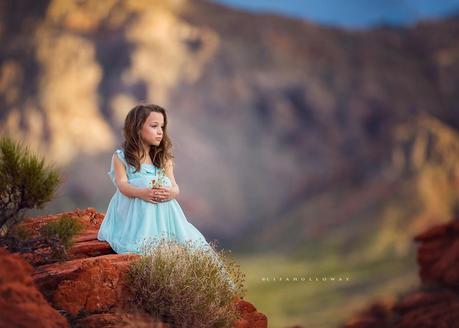 photo de Lisa Holloway représentant une jeune fille en robe bleu pale assise sur un rocher 