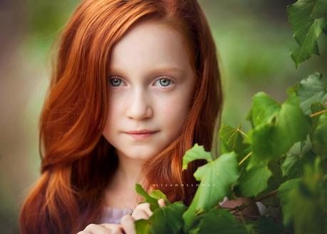 photo de Lisa Holloway représentant le portrait d'une jeune fille rousse derrière des feuilles d'arbre