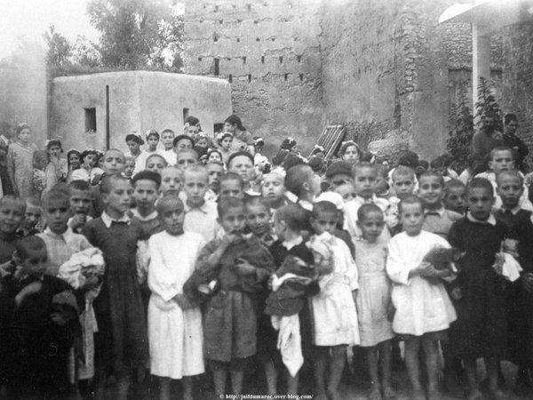 Distribution de vêtements aux élèves de l’École de Sidi Rahal 1949. Derrière les tables, de droite à gauche : Mme et M. Goldenberg, M. Elkaïm, de la Communauté israélite de Marrakech, la présidente de l’œuvre d’habillement, Mme Harrus, l’instituteur, puis les membres de la Communauté de Sidi Rahal. Devant, les élèves de l’école.