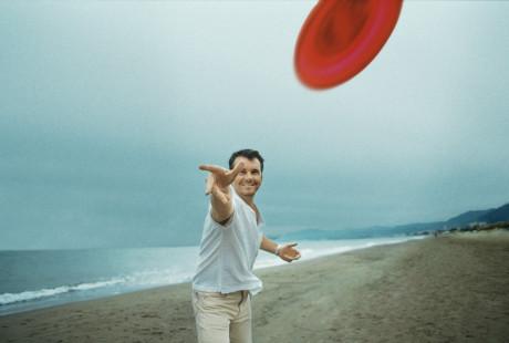 Man throwing a flying disc at the camera on the beach