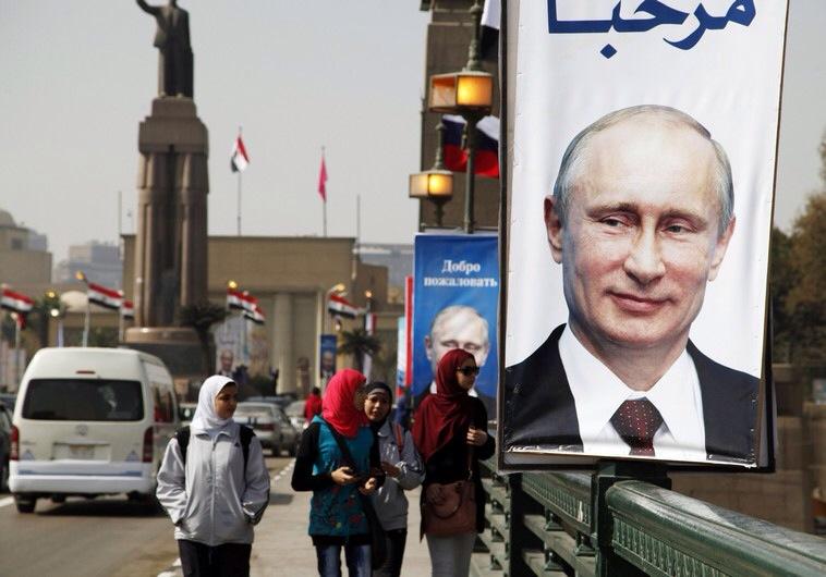 Girls walk past a banner with a picture of Russian President Vladimir Putin along a bridge, in central Cairo
