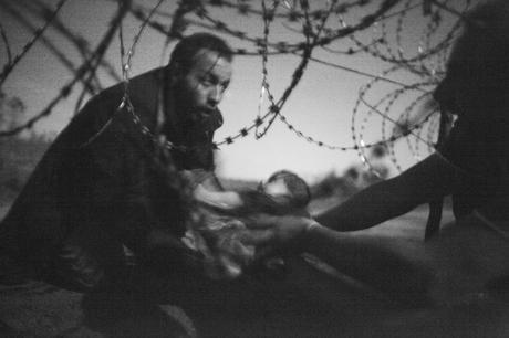 Prix Photo de l’année 2015 – World Press Photo Warren Richardson, Australie Espoir d’une nouvelle vie, 28 août, Frontière serbo-hongroise. 28 août 2015. Un bébé est remis à travers des fils barbelés à un réfugié syrien parvenu à traverser la frontière séparant la Serbie de la Hongrie, près de Röszke. La Hongrie durcissait sa position à l’égard des réfugiés tentant d’entrer dans leur pays. Dès juillet, ce pays avait amorcé l’implantation d’une clôture de quatre mètres longeant sa frontière avec la Serbie, scellant ainsi le pays, à l’exception de ses routes officielles. Les réfugiés ont tenté plusieurs moyens de passer avant la finalisation de la clôture, le 14 septembre. Durant cette nuit-là, le groupe avait passé quatre heures, dissimulé dans un verger, tentant d’éviter les barrages policiers et le poivre de Cayenne, tout en essayant de se frayer un chemin. 