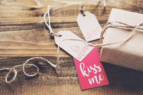 Paper tags with “kiss me” written on one of them next to a wrapped gift