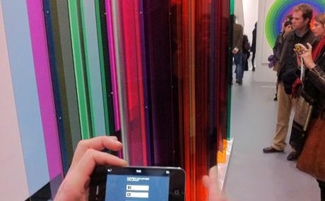 Plusieurs visiteurs en train d’interagir avec leur smartphone, face à « Transchromie mécanique » (1965) de Carlos Cruz-Diez.