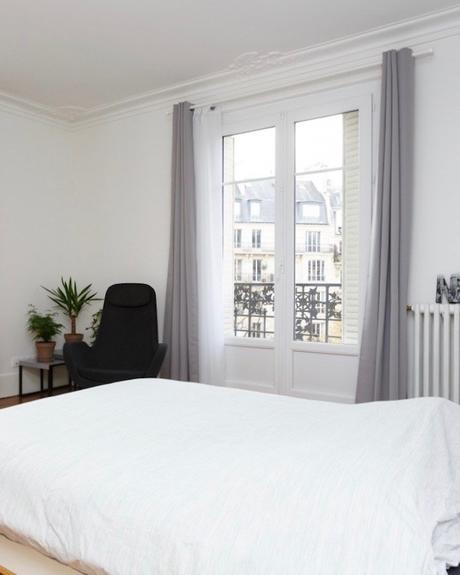 appartement chic parisien chambre lit draps blancs fauteuil noir rideaux gris plante verte petit balcon - blog déco - clemaroundthecorner
