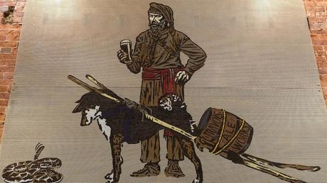 Une œuvre d'art montre un homme du temps des explorateurs, une bière à la main et un chien portant un tonneau de bière.