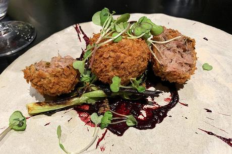 Canard confit cuit lentement aux cinq épices et frit au panko avec cerise noire, oignons de printemps carbonisés et poudre d'olive chez Brunel's