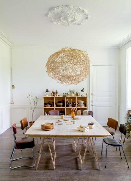 salle à manger table bois avec tréteaux chaises vintage en cuir suspension fibres naturelle moulures au mur