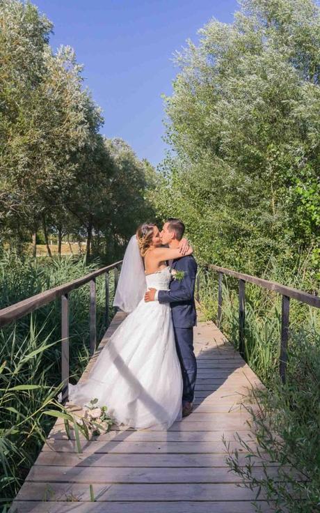 Les mariés s'embrassent sur un pont traversant une rivière de roseaux.