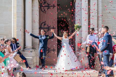 Extrait du mariage de Samia et Romain à Nîmes les mariés sortent triomphalement de l'église, levant les bras sous une pluie de confettis rouges en forme de coeur