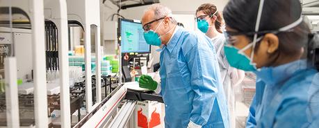 Photo de trois chercheurs portant des masques, des lunettes de sécurité et des blouses dans un laboratoire 