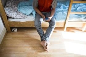 Homme assis sur un lit superposé avec téléphone portable
