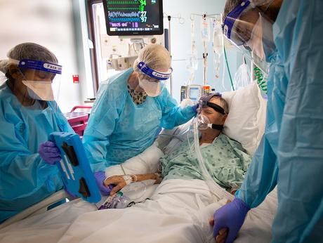 Un homme qui finirait par mourir de COVID est entouré d'infirmières, dont l'une lui tient la main