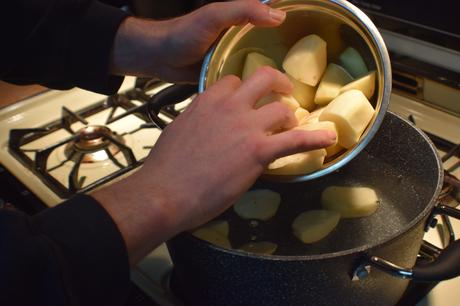 Des mains d'homme mettent des pommes de terre coupées dans une casserole d'eau.