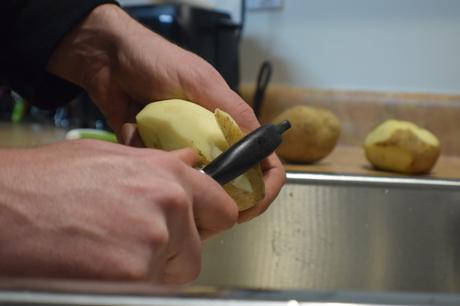 Mains épluchant des pommes de terre dans un évier avec un porte-patates.