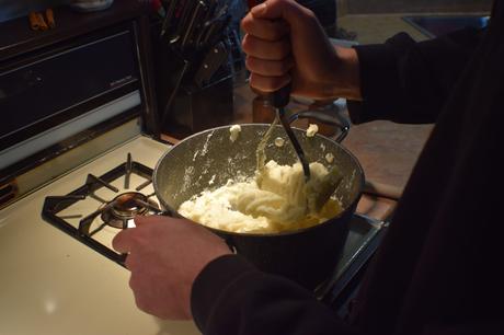 Un homme en pull qui écrase des pommes de terre avec un presse-purée.