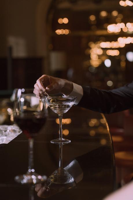 Bases, conseils et astuces du barman homme en costume remuant un martini dans un bar