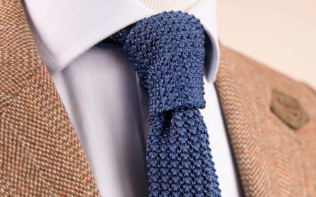 Gros plan sur une cravate bleue en tricot portée avec une chemise et une veste Cravate en tricot bleue portée par un mannequin en bois avec une chemise blanche et une veste en tweed beige